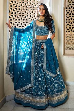 a woman in a blue and gold lehenga standing next to a white wall