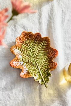 a leaf shaped dish sitting on top of a white table cloth next to some flowers