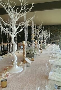 the tables are set up for an elegant wedding reception with white trees and crystal beaded place settings