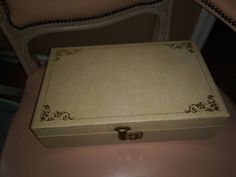 an empty white box sitting on top of a pink table next to a chair with beaded trim around the edges