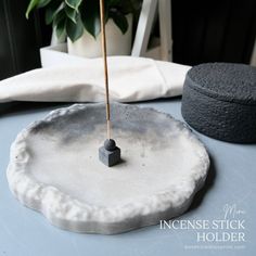 an incense stick is placed on top of a white plate with a small black object in the middle