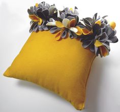 a yellow pillow with grey and white flowers on the front, sitting on a white surface