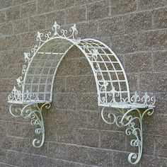 two white wrought iron wall shelves against a brick wall, one with an arched top