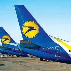 several airplanes are parked on the tarmac at an air port run way, one is blue and yellow