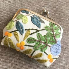 a white purse with colorful flowers and leaves on the front is sitting on a gray surface