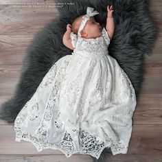 a baby in a white dress is laying on a black and gray rug with her hands behind her head