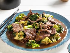 a blue plate topped with beef and broccoli covered in brown sauce next to chopsticks