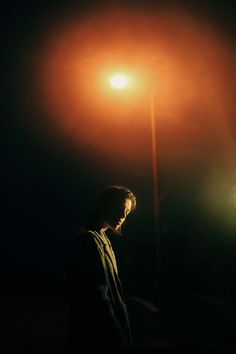 a man standing in the dark under a street light with his head turned to the side