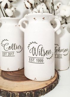 three white vases with cotton flowers in them on a wooden stand next to the wall