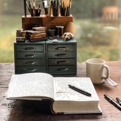 an open book sitting on top of a wooden table next to a cup and pen