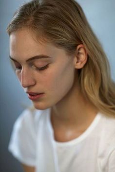 a woman with long blonde hair wearing a white t - shirt and looking down at her cell phone