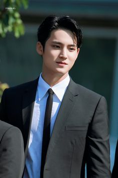 a young man in a suit and tie standing next to another person wearing a white shirt