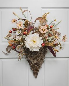 an arrangement of flowers is hanging on the front door with a heart - shaped wreath