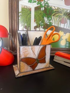 a desk with scissors, pencils and pens in a holder next to a window