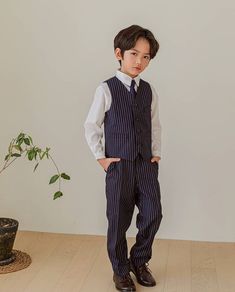 a young boy wearing a suit and tie standing in front of a potted plant