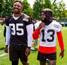 two football players in black and orange jerseys walking on the field with one wearing a hoodie