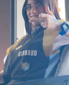 a woman with glasses pointing to the side and wearing a vest that says girbaud