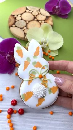 a hand holding an easter egg decorated with orange and white flowers on top of a table