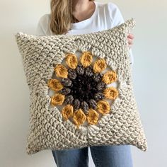 a woman holding a crocheted pillow with an orange flower