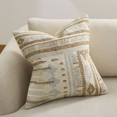 a close up of a pillow on a couch with a white chair in the background