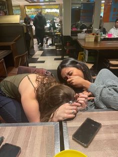 two women sitting at a table with their hands on each other's head and one woman covering her eyes