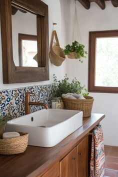 a white sink sitting on top of a wooden counter next to a mirror and potted plants