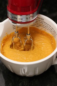 a red mixer is mixing yellow batter in a white bowl on a black countertop