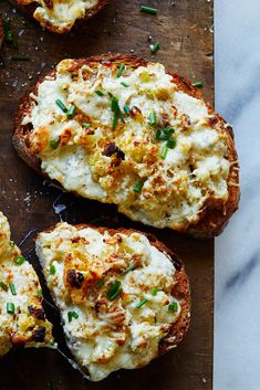 three pieces of bread topped with cheese and chives on a wooden cutting board next to other food items