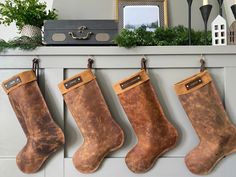 three christmas stockings hanging from hooks in front of a mantel with candles and greenery