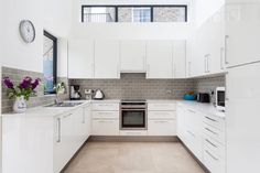 a kitchen with white cupboards and appliances in it's center island, along with a clock mounted on the wall