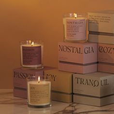 several candles are stacked on top of each other in front of the box that says, nostal gia cozy