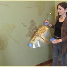 a woman standing in front of a wall holding a paint roller and painting the walls