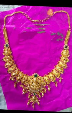 a gold necklace is displayed on a pink cloth in front of a purple bag with the word