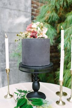 there is a black cake with flowers on it and three candles next to the cake