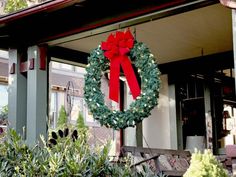 a christmas wreath hanging on the front door of a house with a red bow around it