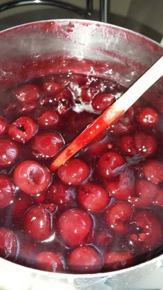 a pot filled with cherries on top of a stove next to a wooden spoon