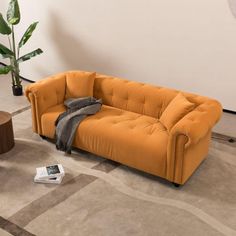 an orange couch sitting on top of a rug next to a wooden table and potted plant