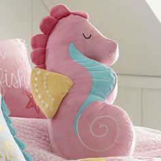 a pink seahorse stuffed animal sitting on top of a bed next to two pillows