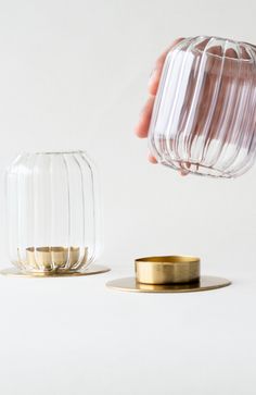 a hand is pouring water into a glass vase next to a gold plated candle holder