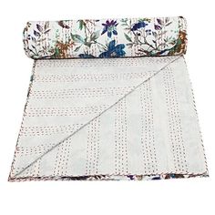 a white and blue flowered blanket laying on top of a tablecloth with an embroidered border