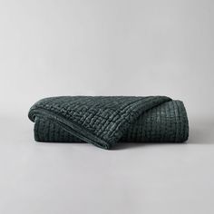 a dark green quilted blanket folded on top of a white table with grey background