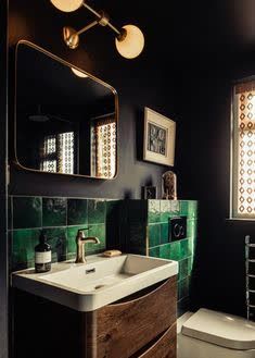 a bathroom with black walls and green tiles on the wall, along with a white toilet