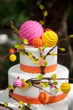 a three tiered cake with flowers and branches on the top is decorated in bright colors