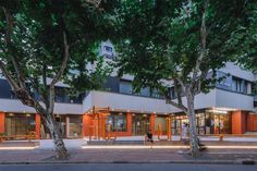 an empty street in front of a building with trees on both sides and people walking by