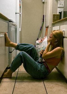 a woman sitting on the floor next to a refrigerator