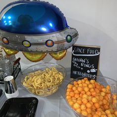 a table topped with lots of food next to a sign and balloon shaped like an spaceship