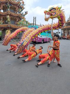 people in orange and yellow outfits are performing with dragon dance equipment on the street while another person is holding a flag