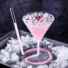 a pink drink sitting on top of ice with a straw in the glass next to it