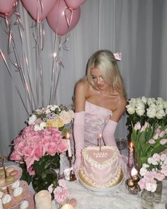 a woman sitting in front of a cake with candles on top of it, surrounded by flowers and balloons