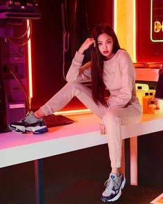 a woman sitting on top of a table next to a computer keyboard and mouse in a room with neon lights